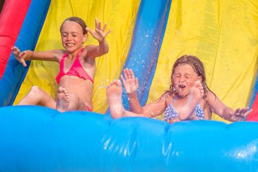 Sisters sliding down an inflatable slide making a splash.